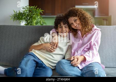 Happy mother and son sitting on sofa in living room at home Stock Photo
