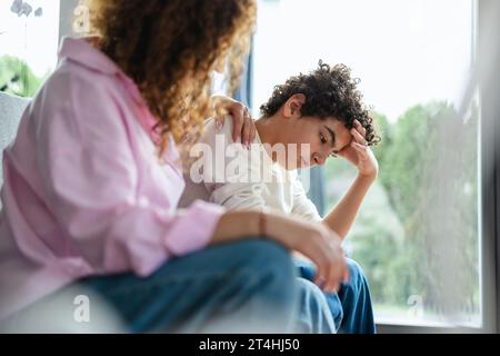 Upset boy sitting on sofa while his mother looking at him Stock Photo