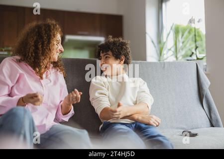 Happy mother and son sitting on sofa in living room at home Stock Photo