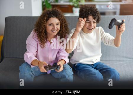 Mother and son playing video games while sitting on sofa at home Stock Photo