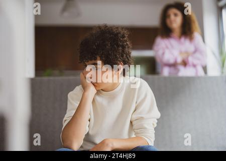 Upset boy sitting on sofa while his mother looking at him Stock Photo