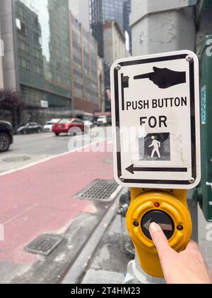 crosswalk, female hand pushing button for crosswalk in street of New York. Crosswalk push button and sign with selective focus on street pole. Traffic Stock Photo