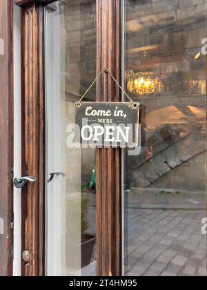 open sign, vintage come in we are open entrance sign hanged on a window door of a small shop or store. entrance of a cafe or shop with sign. small bus Stock Photo