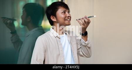 Smiling asian guy using phone voice recognition to send message Stock Photo
