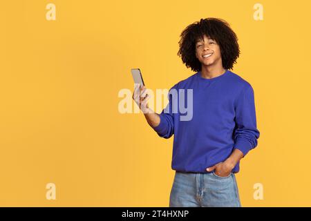 Happy Young Black Guy Using Mobile Phone And Smiling At Camera Stock Photo