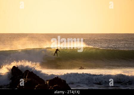 A surfer navigating a large wave in the ocean at sunset on a beautiful, clear day in Punta de Lobos Stock Photo