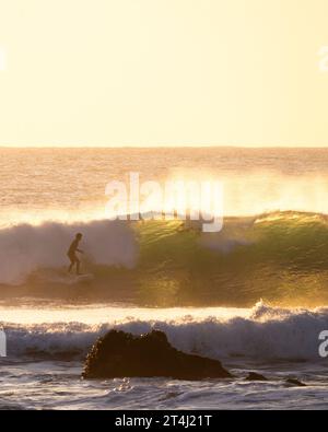 A surfer navigating a large wave in the ocean at sunset on a beautiful, clear day in Punta de Lobos Stock Photo