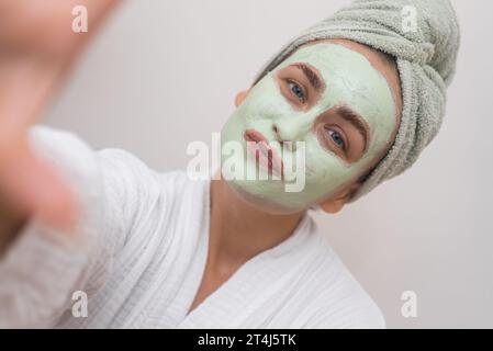 Joyful Snapshot: in a bathrobe, she takes selfie with clay mask, exuding happiness in every pixel. Stock Photo