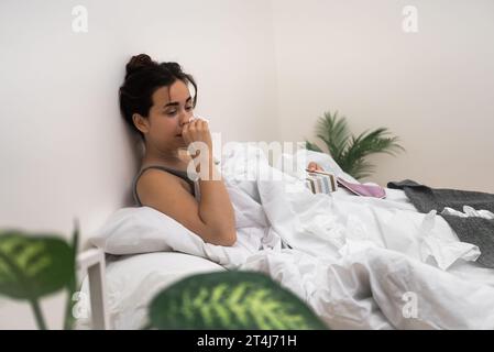 Battling illness, she sits in bed, using tissues and medical drops to alleviate her symptoms Stock Photo