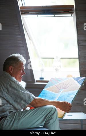 Man, artist or holding painting with pride in bedroom and happy elderly guy by window for creative art. Mature painter, design or retirement for Stock Photo