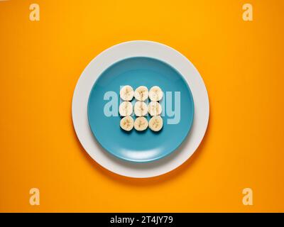Sliced bananas on a plate over yellow background. Top view, copy space. Creative food concept. Stock Photo