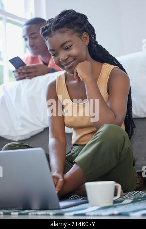 Young african american man and woman sitting in the bedroom smiling and using wireless devices. Black couple using a laptop and phone on a weekend Stock Photo