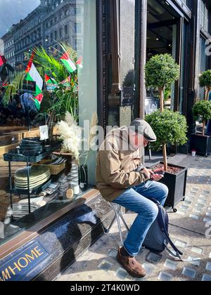 Shop window reflections. An elderly male checks his iphone as the demonstrators march down Regent street,  London 14th October 2023. Stock Photo