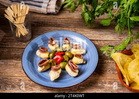 Cantabrian anchovies on artichoke hearts on a plate accompanied by olives and chips. Stock Photo