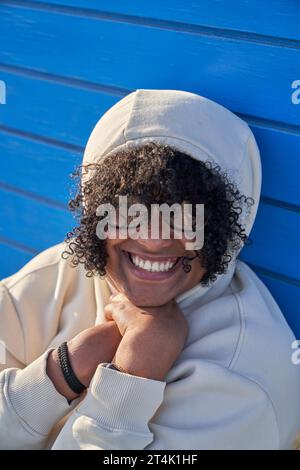Black woman dressed in a beanie sweatshirt and afro hair on a blue background on a sunny day Stock Photo
