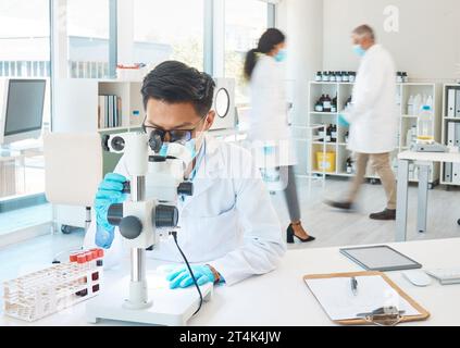 Focused and determined even amongst the hustle and bustle. a young scientist using a microscope while working in a busy lab. Stock Photo