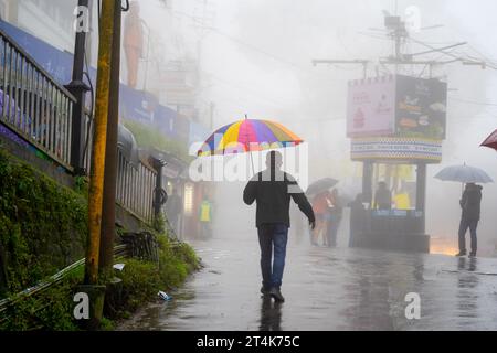 Man carrying colorful umbrella along the fog covered streets of darjeeling west bengal showing the natural beauty of the town Stock Photo