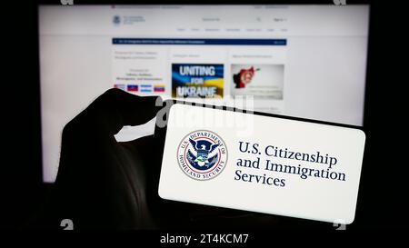 Person holding cellphone with seal of American agency Citizenship and Immigration Services (USCIS) in front of webpage. Focus on phone display. Stock Photo
