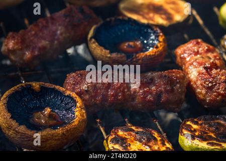 Grilling meat rolls called mici or mititei with vegetables on char barbecue. Charcoal grill with burning fire Stock Photo