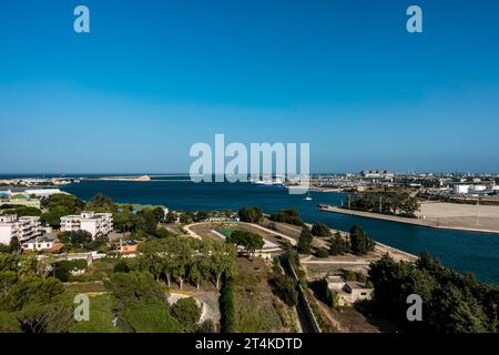 Aerial view of Brindisi, Italy, showing the Adriatic Sea, harbor, ferry terminal, residential buildings, and trees under a clear blue sky. Stock Photo