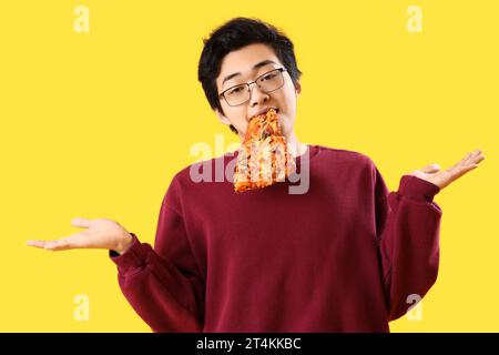 Young Asian man eating tasty pizza on yellow background Stock Photo