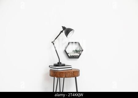 Desk lamp on small wooden table and florarium near white wall Stock Photo