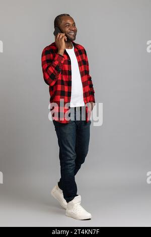 Happy black bearded man wearing red checkered shirt talking on smartphone Stock Photo
