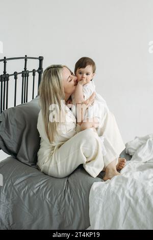 Mother and daughter in bed, happy mother tenderly hugs and kisses her child. Taking care of the child. Vertical frame. Stock Photo