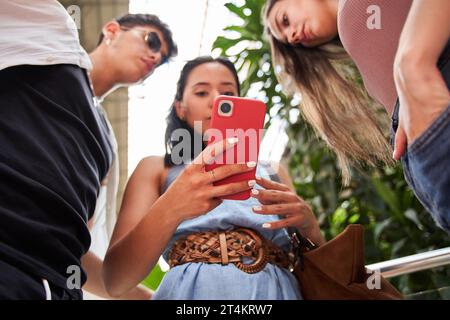 selective focus. three young students looking at cell phone from below. latina woman showing her cell phone to her friends. Stock Photo