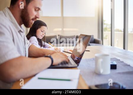 Father working from home on his laptop. Freelancer dad using laptop while child does schoolwork. Parent working remotely and looking after child Stock Photo