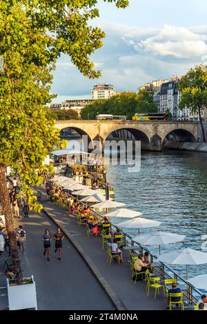 Lively quay along the Seine river with people enjoying time outside, relaxing and running, in summer, Paris city centre, France Stock Photo