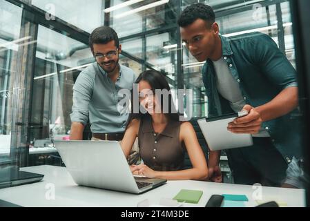 Business people. Group of three young and cheerful employees using modern technologies while working in modern office. Job concept Stock Photo