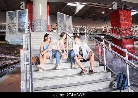 Portrait of diverse college friends sitting on station stairs - Happy multiracial group of young people having fun and relaxing - Friendship, youth an Stock Photo