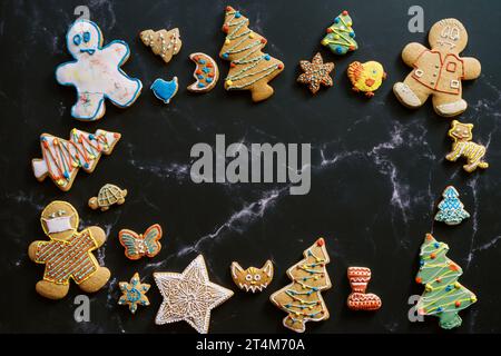 Christmas glazed cookies lie around the perimeter of a dark marble background with white veins Stock Photo
