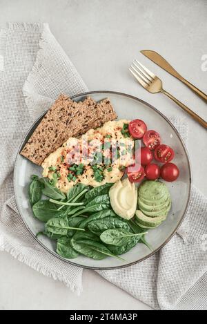 Scramble eggs with cherry tomatoes, fresh spinach leaves, avocado and crispbreads on a plate, top view Stock Photo