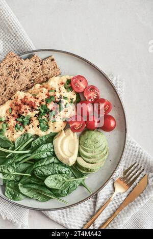 Scramble eggs with cherry tomatoes, fresh spinach leaves, avocado and crispbreads on a plate, top view Stock Photo