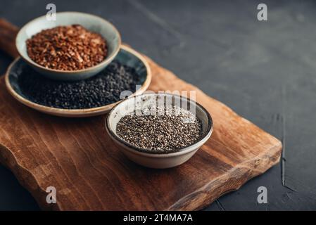 Black sesame, flax and chia seeds in ceramic plates on a dark background Stock Photo