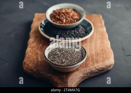 Black sesame, flax and chia seeds in ceramic plates on a dark background Stock Photo