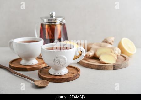 Ginger tea with lemon in a white cups with ginger root  on cutting board and teapot on a light background closeup Stock Photo