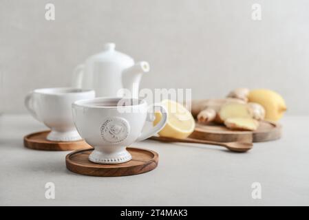 Ginger tea with lemon in a white cups with ginger root  on cutting board and teapot on a light background closeup Stock Photo