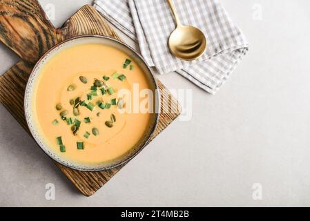 Pumpkin soup in a bowl with pumpkin seeds, green onions and breadsticks on a light background, top view Stock Photo