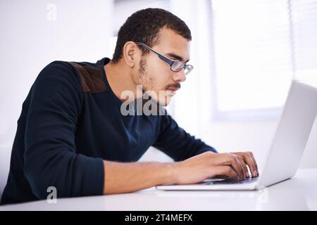 Blazing through lines of code with ease. a handsome young man working on his laptop in an office. Stock Photo