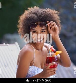 Loving the cocktails and sunshine. Attractive ethnic female posing with sunglasses and fruity cocktail. Stock Photo