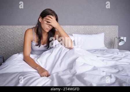 Getting a slow start this morning. an attractive young woman sitting on her bed looking unhappy. Stock Photo