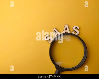 Magnifying glass and wooden word with text SAAS on a yellow background. Stock Photo