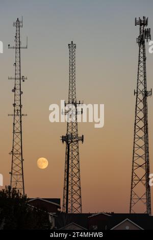 Three cell towers with the moon during sunset. Communications modern portrait concept. Stock Photo