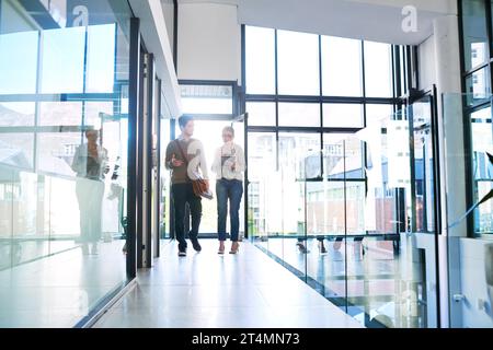 Striving towards success together. two businesspeople using a digital tablet together while walking in an office. Stock Photo