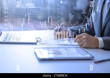 Businessman standing in the office reviewing financial annual reports with modern tablet and laptop computer for a return on investment. Stock Photo