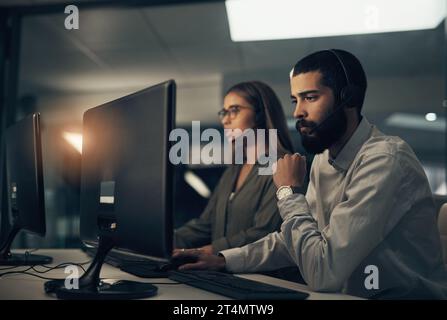 Let me look into it for you. a call centre agent working in an office alongside a colleague at night. Stock Photo