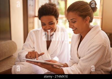 Lets get this therapy started...two friends in bathrobes using a digital tablet at a spa. Stock Photo